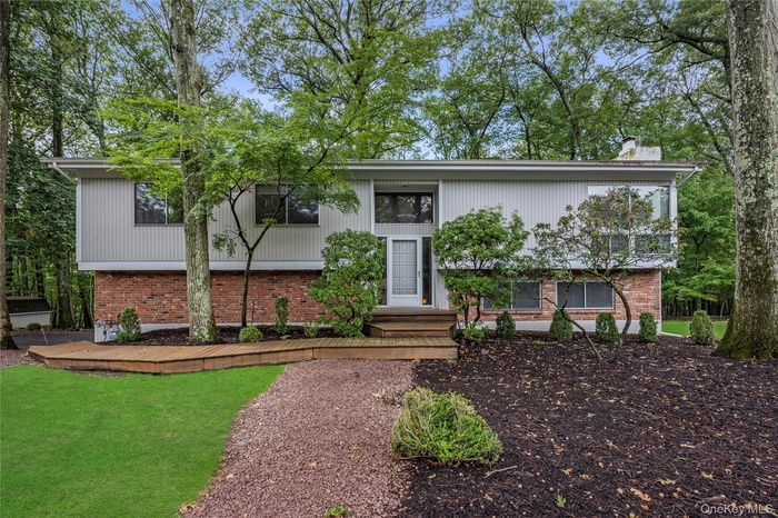 Bi-level home featuring a chimney, a front yard, and brick siding