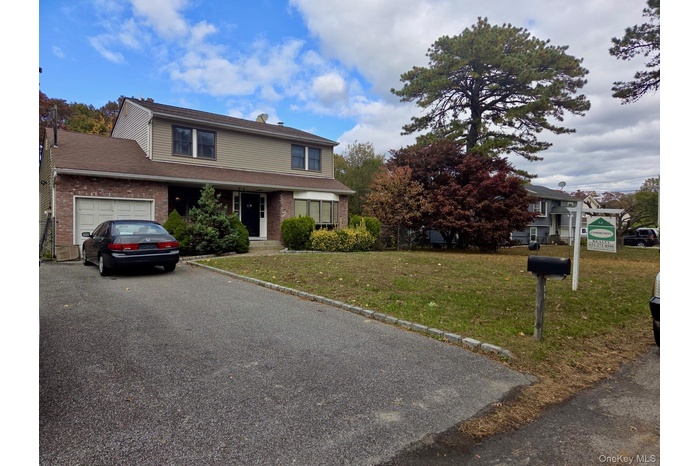 Traditional-style house with a front yard, a garage, brick siding, asphalt driveway, and a shingled roof