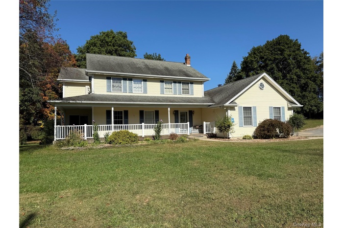View of front of property with covered porch, a chimney, a front lawn, and roof with shingles