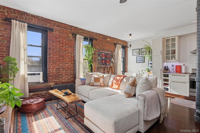 Living area featuring wood-type flooring, radiator heating unit, and brick wall