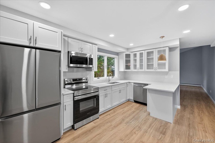 Kitchen featuring glass insert cabinets, stainless steel appliances, white cabinets, recessed lighting, and light wood-type flooring