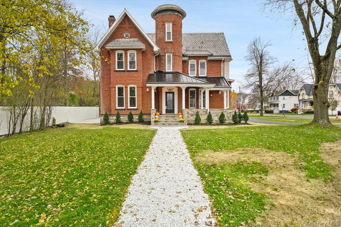 Victorian home featuring a chimney, brick siding, and covered porch