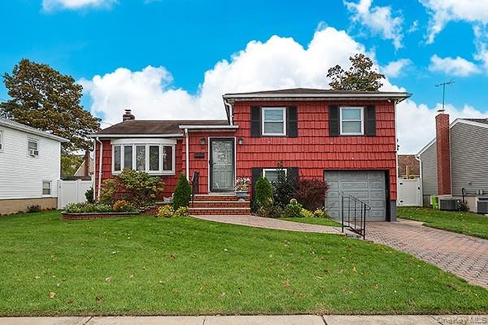 Split level home with decorative driveway, a garage, and a chimney