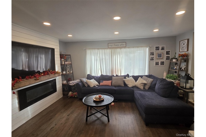 Living room featuring dark wood-style floors, recessed lighting, and a glass covered fireplace