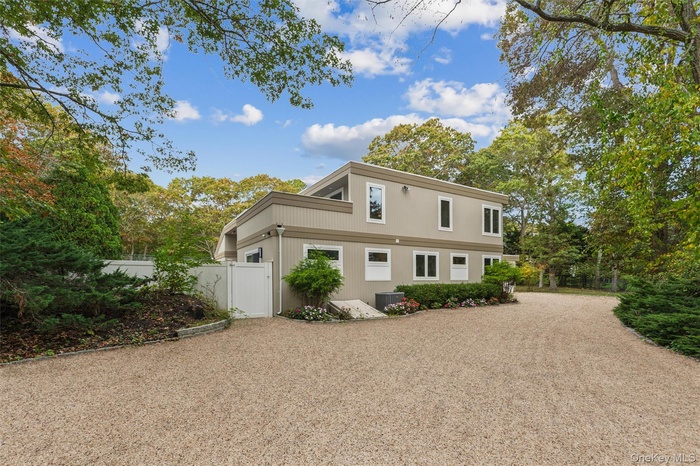 View of side of home featuring gravel driveway and view of wooded area