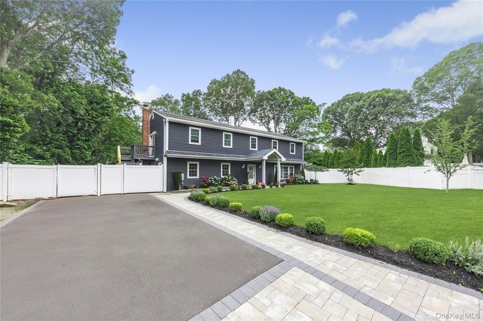 Colonial house with a fenced backyard, a chimney, view of scattered trees, and a gate