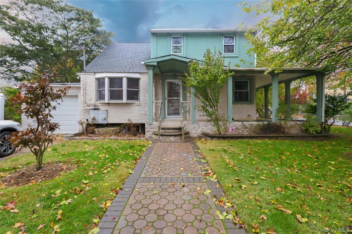 View of front of property with a front lawn, brick siding, a porch, and a garage