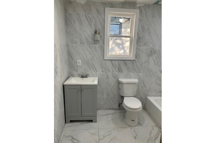 Bathroom featuring tile walls, vanity, light marble finish flooring, and a tub