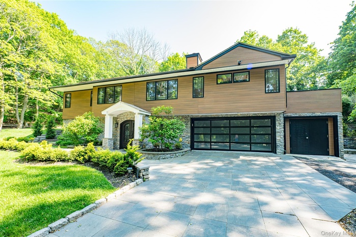 View of front facade featuring stone siding, a garage, concrete driveway, and a chimney