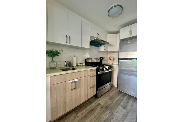 Kitchen featuring stainless steel appliances, range hood, light wood-type flooring, light brown cabinetry, and backsplash