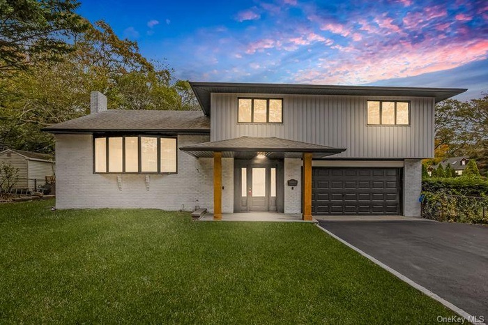 View of front of house with a porch, asphalt driveway, a chimney, a front lawn, and brick siding