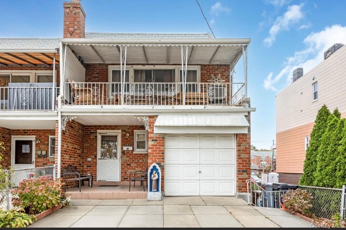 View of front facade featuring brick siding, a balcony, driveway, and a garage
