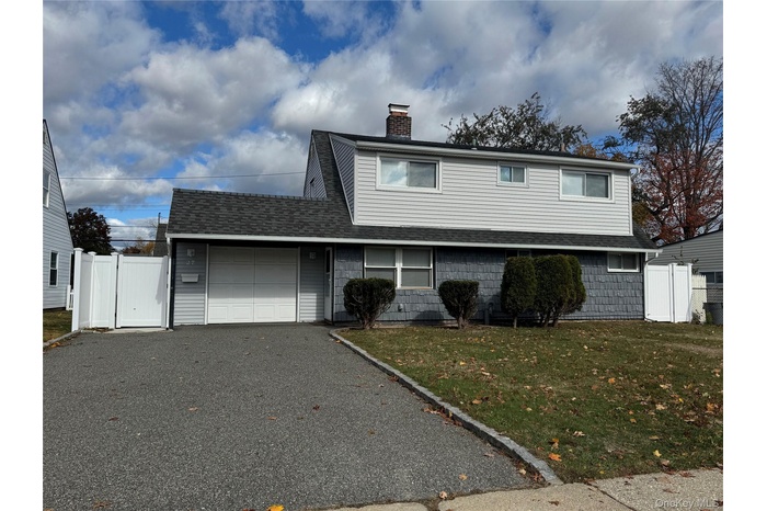 Traditional-style house featuring a shingled roof, a garage, driveway, a chimney, and a gate