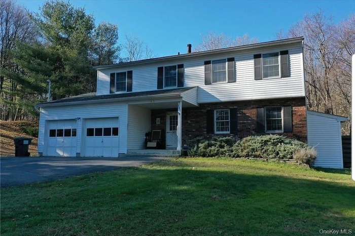 Traditional home featuring covered porch, a garage, a front yard, brick siding, and driveway