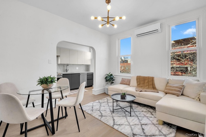 Living room featuring arched walkways, light wood finished floors, a wall mounted AC, and a chandelier