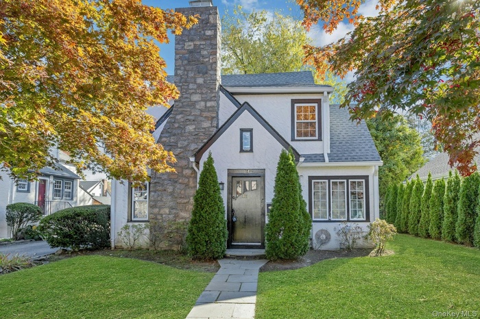 Tudor house featuring a chimney, stucco siding, and shingled roof.