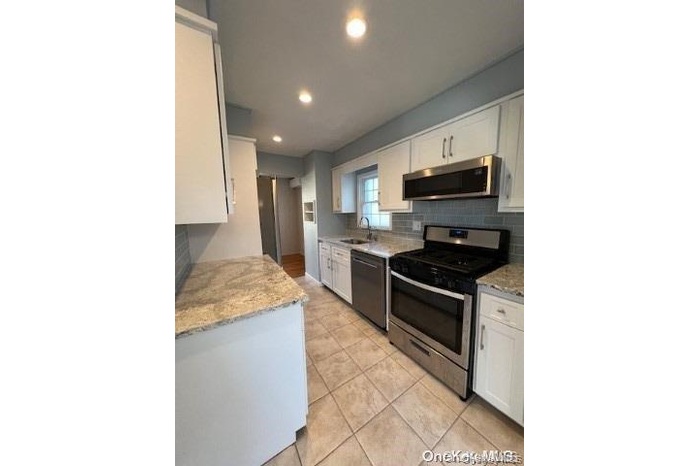 Kitchen featuring backsplash, white cabinetry, appliances with stainless steel finishes, light stone counters, and recessed lighting