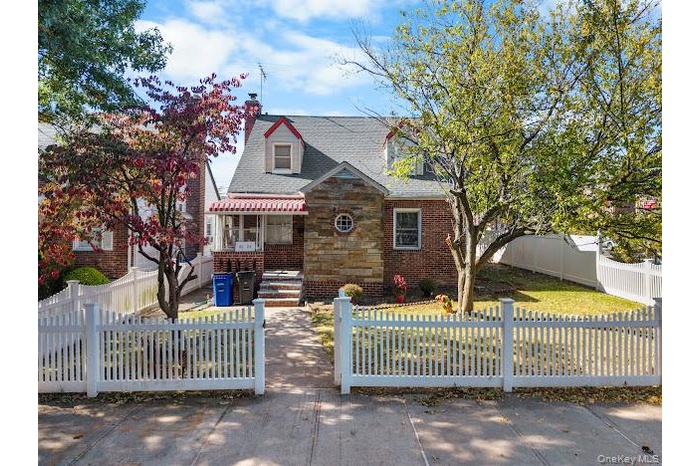 View of front facade with a fenced front yard, a gate, a chimney, stone siding, and roof with shingles