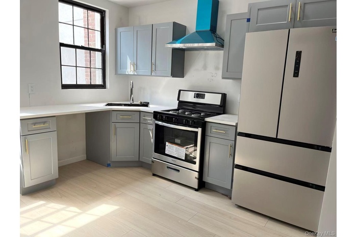 Kitchen featuring freestanding refrigerator, stainless steel range with gas stovetop, gray cabinetry, wall chimney exhaust hood, and light wood-style 