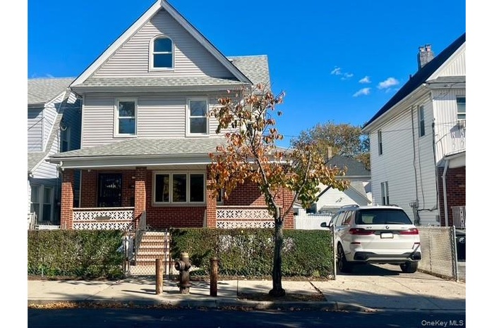 View of front of home featuring covered porch, a shingled roof, brick siding, and stairway