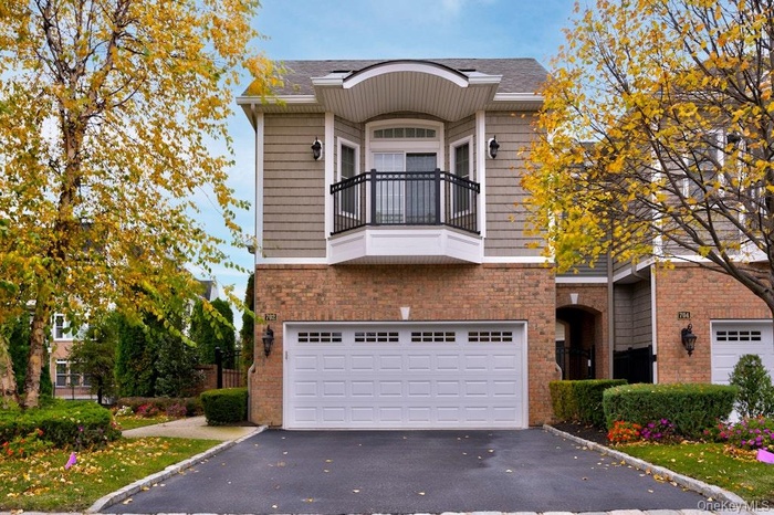View of front of home featuring a balcony, asphalt driveway, an attached garage, brick siding, and a shingled roof