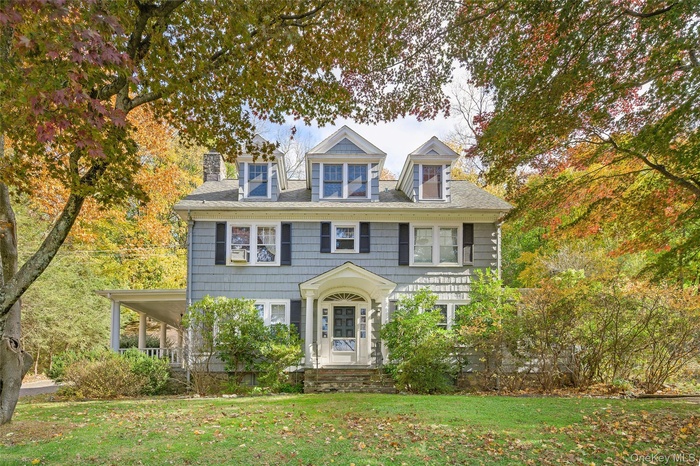 View of front of home with a front lawn, a chimney, and covered porch