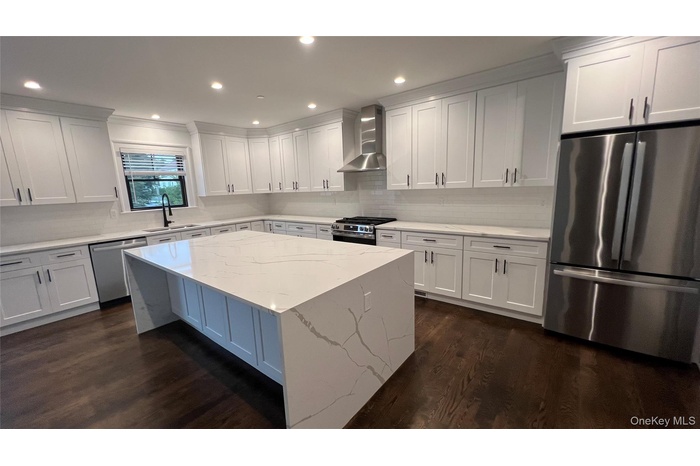 Kitchen featuring stainless steel appliances, a kitchen island, light stone counters, wall chimney exhaust hood, and recessed lighting