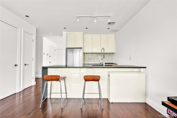 Kitchen featuring backsplash, cream cabinets, freestanding refrigerator, dark wood-type flooring, and a kitchen bar