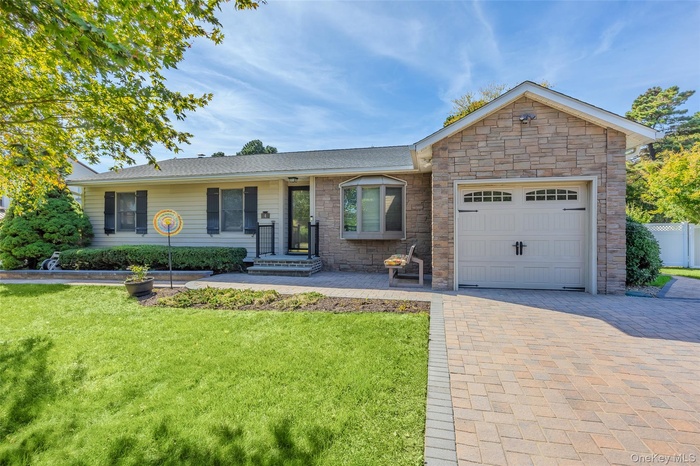 Single story home with a front yard, an attached garage, decorative driveway, and stone siding