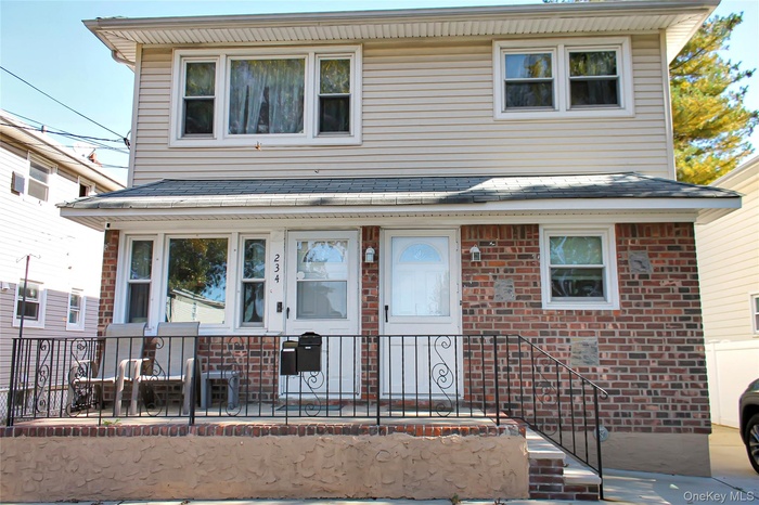 View of front facade featuring brick siding, a porch, and roof with shingles