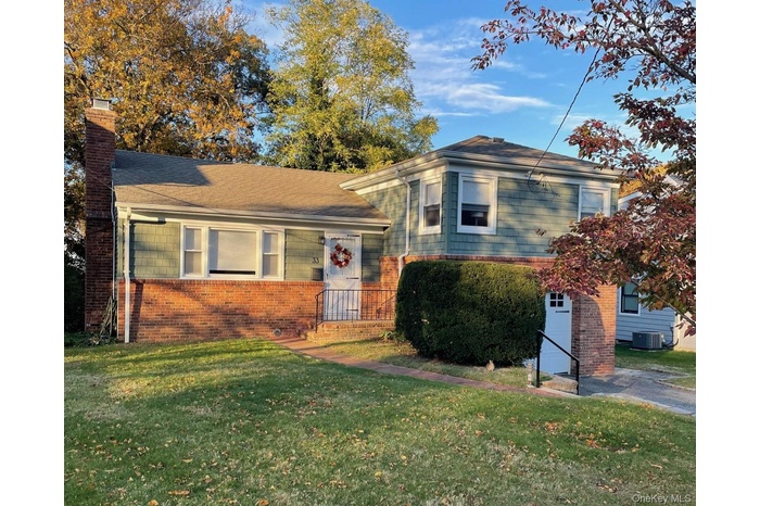 Tri-level home with brick siding, a chimney, and a front lawn