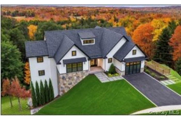 View of front of property featuring a front yard, a wooded view, covered porch, and driveway