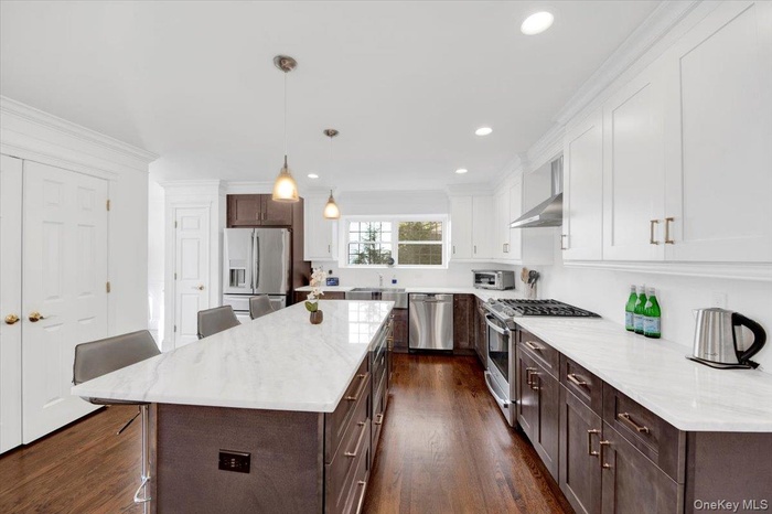 Kitchen featuring a breakfast bar, dark brown cabinets, stainless steel appliances, hanging light fixtures, and recessed lighting