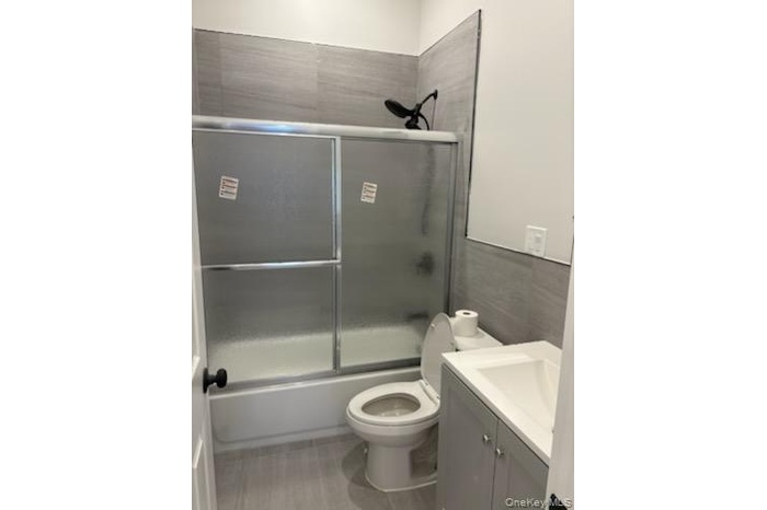 Bathroom featuring vanity, bath / shower combo with glass door, and tile walls