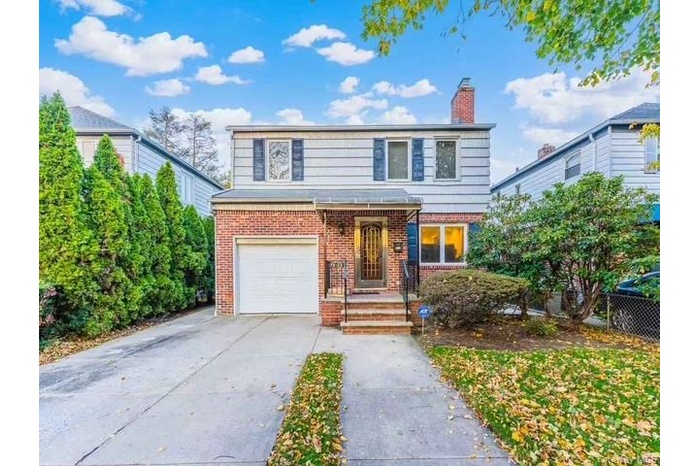 Traditional-style home featuring brick siding, a garage, a chimney, and driveway