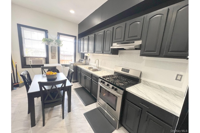 Kitchen featuring under cabinet range hood, gas stove, cooling unit, decorative backsplash, and light marble finish flooring