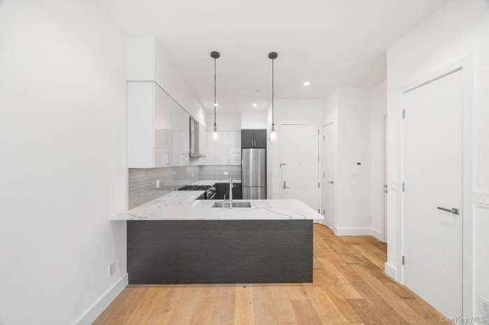 Kitchen with backsplash, modern cabinets, a peninsula, light wood-type flooring, and pendant lighting