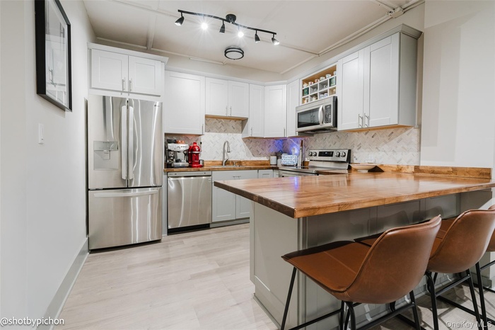 Kitchen with butcher block counters, decorative backsplash, stainless steel appliances, a breakfast bar, and a peninsula