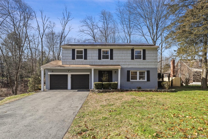 Traditional-style home with solar panels, brick siding, driveway, a front yard, and an attached garage