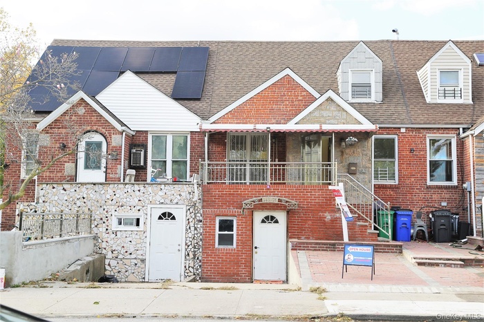 View of front of house featuring a shingled roof, stone siding, brick siding, and a balcony