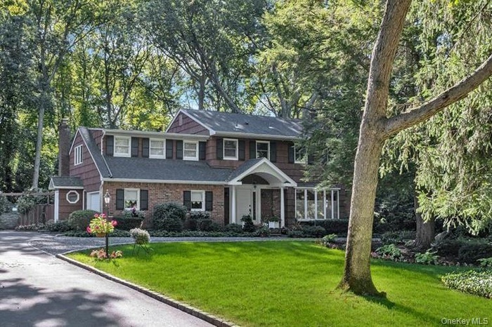 View of front of home featuring a front yard, a garage, driveway, view of wooded area, and roof with shingles