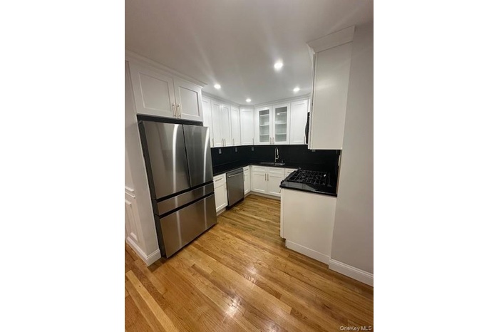Kitchen featuring dark countertops, appliances with stainless steel finishes, white cabinets, light wood-type flooring, and glass insert cabinets