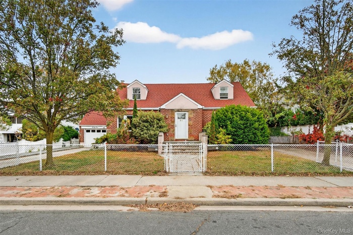 Cape cod-style house featuring a gate, a fenced front yard, brick siding, and driveway