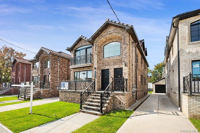 French country style house featuring brick siding, a balcony, a front lawn, an outbuilding, and a detached garage