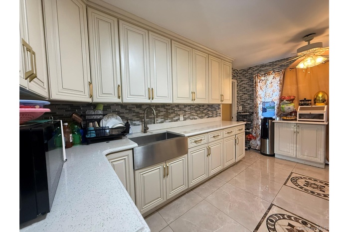 Kitchen with black microwave, light stone countertops, backsplash, light tile patterned floors, and ceiling fan