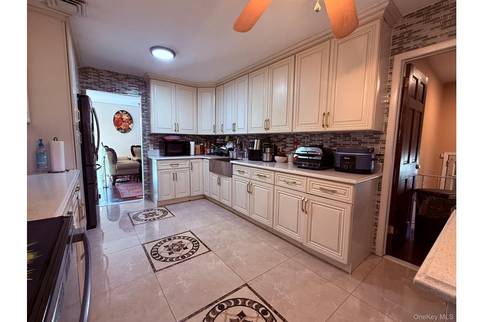 Kitchen featuring black appliances, backsplash, light tile patterned floors, a ceiling fan, and light stone counters