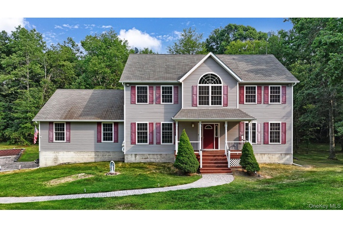 Colonial-style house with a front yard, a shingled roof, a porch, and view of wooded area