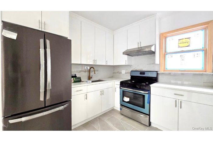 Kitchen featuring stainless steel appliances, white cabinets, under cabinet range hood, and backsplash