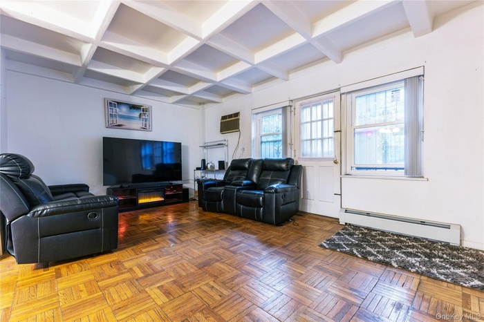 Living area with beamed ceiling, a baseboard heating unit, coffered ceiling, and a wall mounted AC