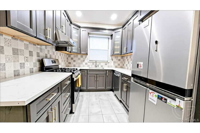 Kitchen featuring stainless steel appliances, glass insert cabinets, light tile patterned flooring, decorative backsplash, and exhaust hood